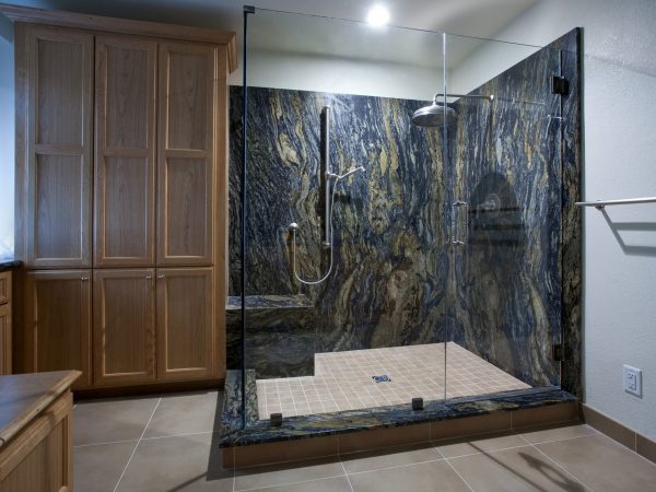 A shower with granite walls, a tile floor, and an overhead rain shower head.