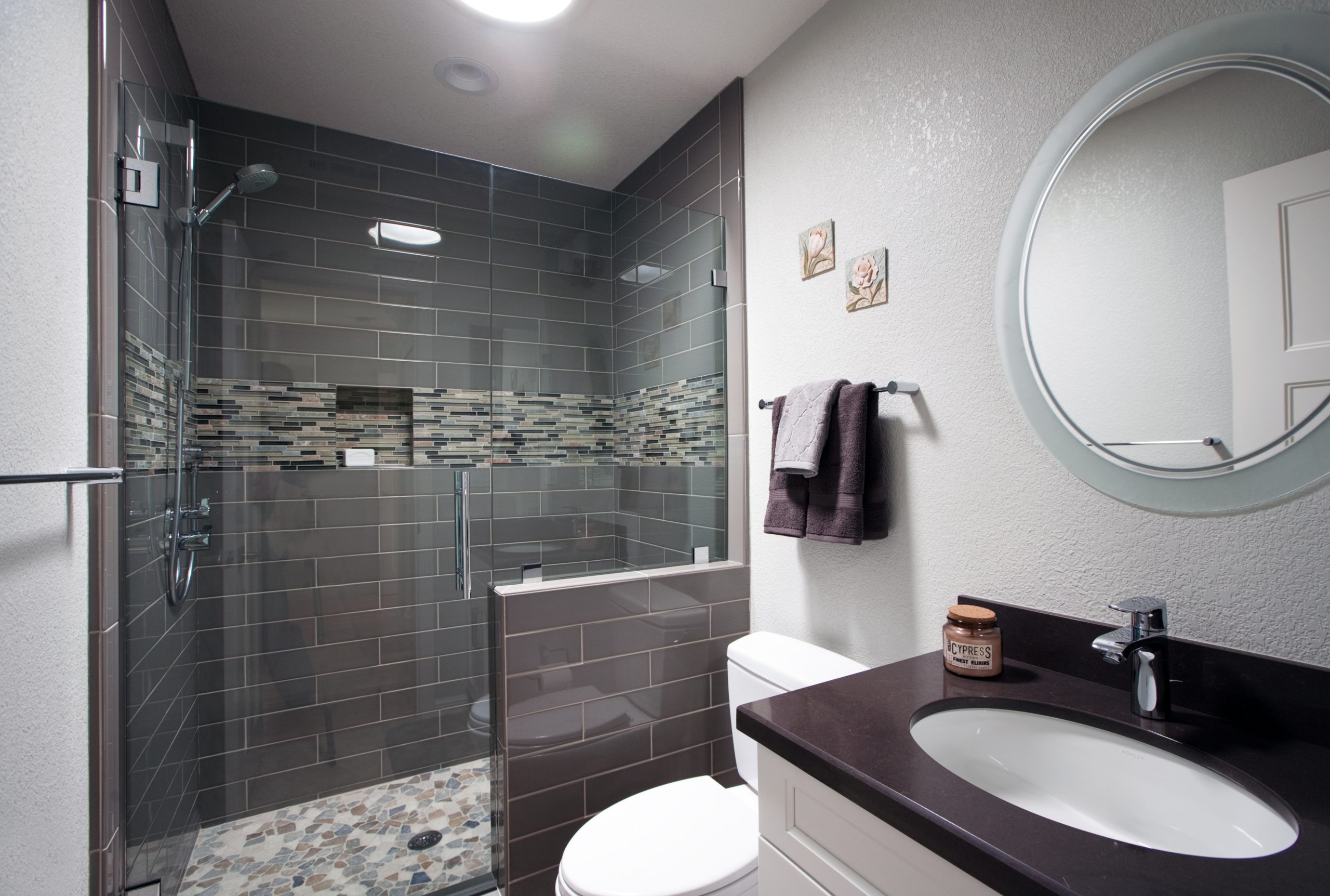 A modern bathroom with grey tile and stone shower floor.
